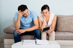 Image of a couple sitting on a couch wondering if they should file Chapter 13 since they've been forced into it.