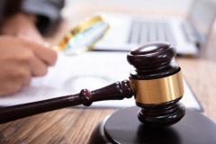 Image of a judge on a virtual hearing, reading notes with the gavel in the foreground and the laptop in the background.