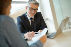 Image of a man with grey hair wearing a suit, and going over paperwork with a woman in a grey sweater.