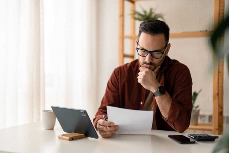 A man sitting in front of his ipad and documents contemplating if he can keep his retirement account by filing bankruptcy.